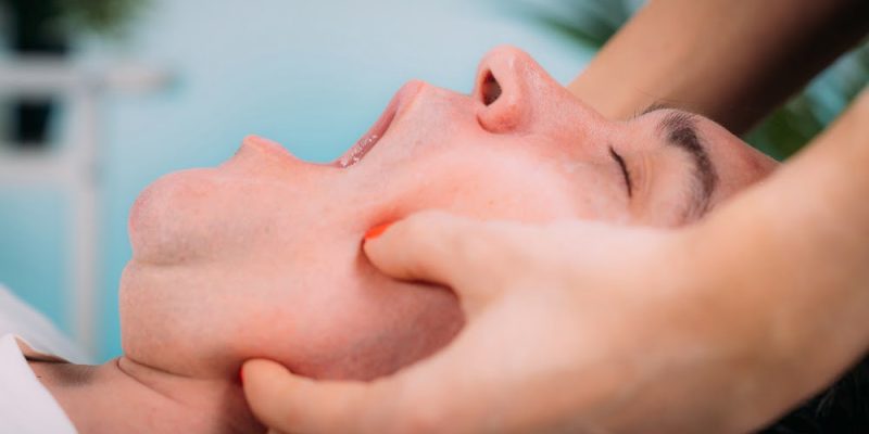 Jaw realignment massage, therapist massaging man’s jaw